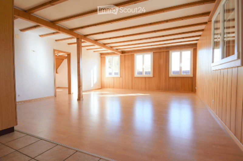 Empty room with wooden flooring, white walls, wooden paneling, and large windows. No furniture or equipment present.