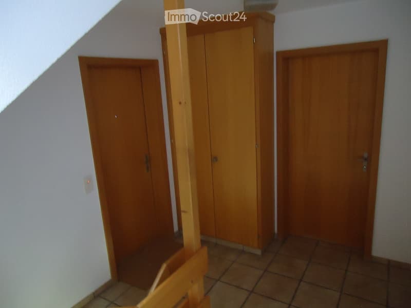 A narrow hallway with wooden doors and a tiled floor, featuring a light switch on the wall and a wooden railing on one side.