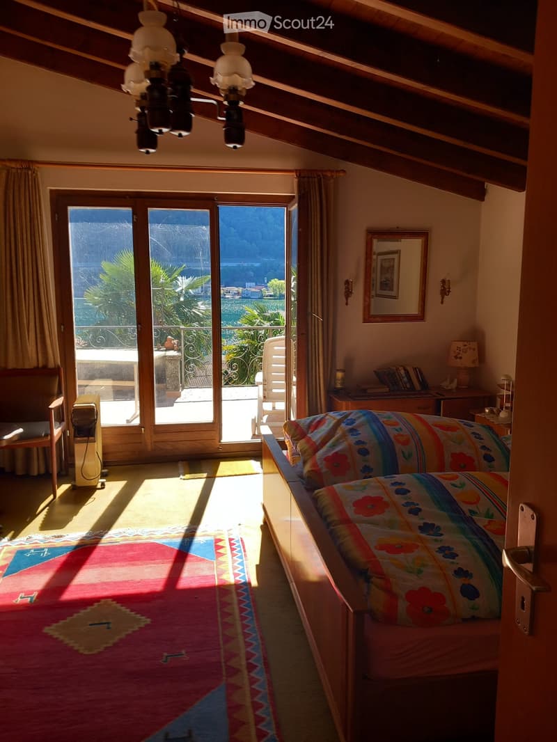 Bright bedroom with wooden beams, large window offering a scenic view, colorful bedspread, patterned rug, and wooden furniture.