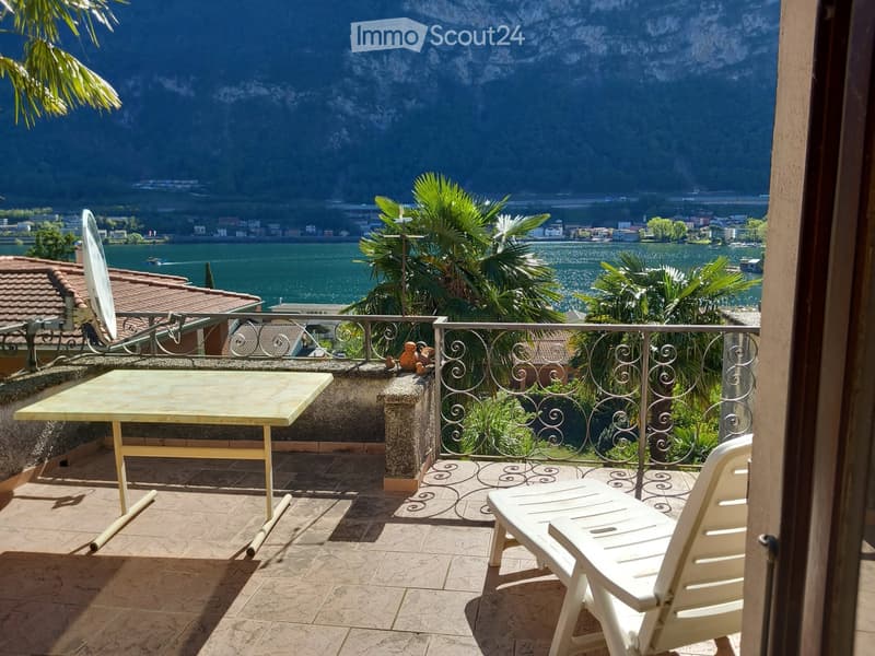 Balcony with a scenic lake and mountain view, featuring a table and a white lounge chair.