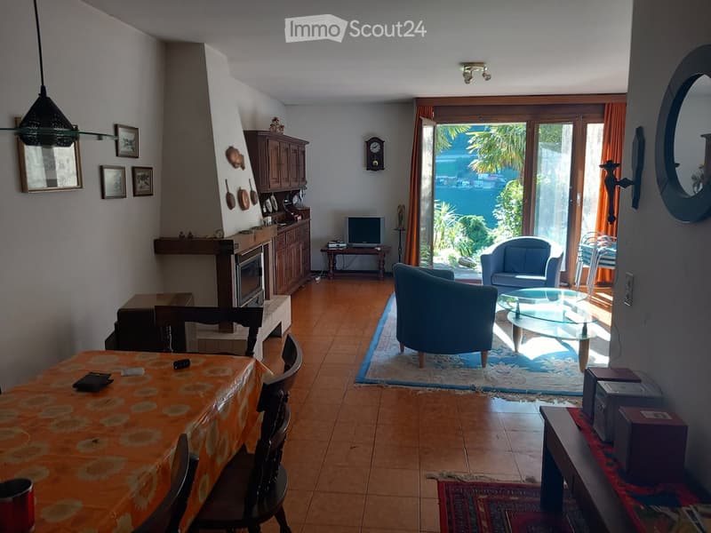 Bright living room with tiled flooring, large glass doors leading to a view, sofa, chairs, coffee table, TV, and fireplace.