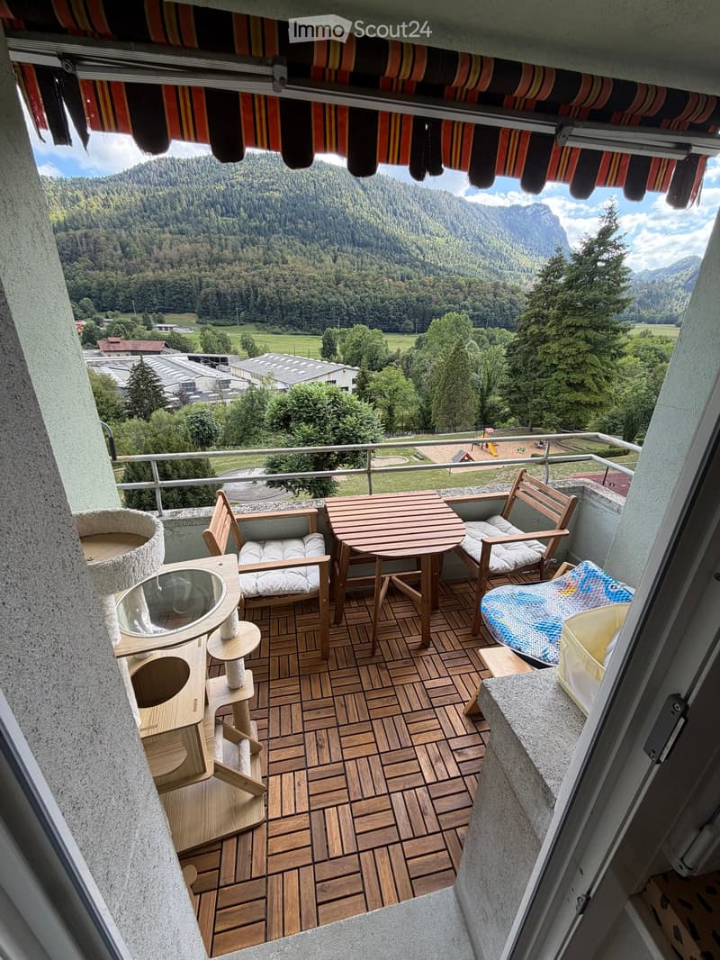 Balcony with wooden decking, table, chairs, and a cat tree, overlooking a scenic mountain landscape.