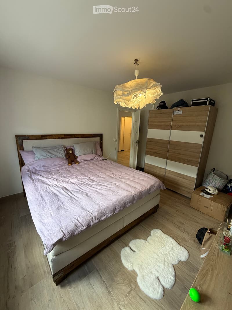 Bedroom with a wooden bed, white bedding, a large wardrobe, a table with a lamp, and a large white teddy bear on the floor.