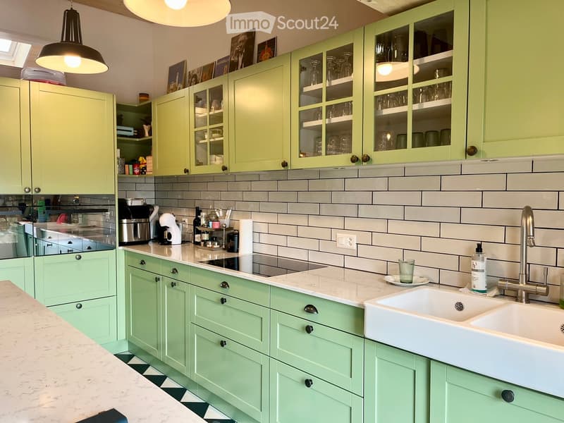 Bright kitchen with mint green cabinets, marble countertops, and a white sink. Visible items include a coffee maker, a cup, and a bottle on the counter.