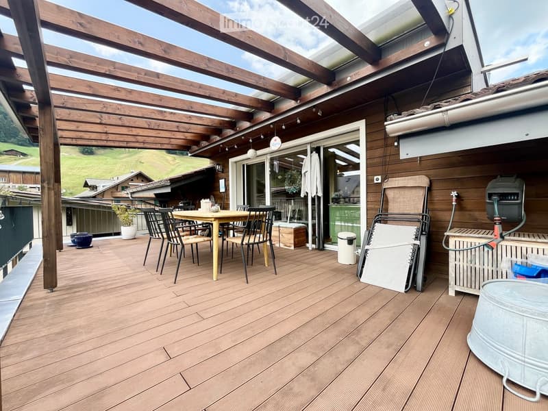 Wooden deck with a table, chairs, a barbecue, and a plant, with a scenic view of the countryside.