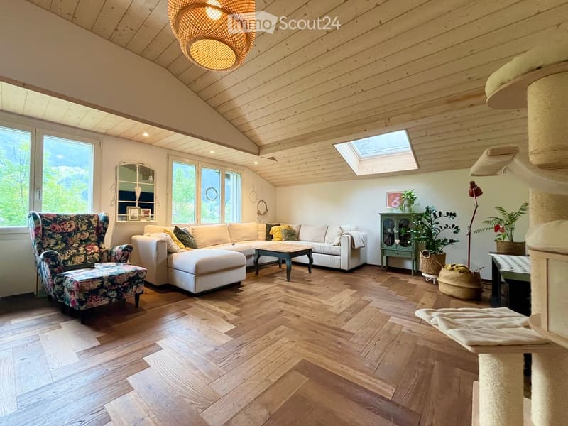 Bright living room with wooden floors, large windows, skylight, white sectional sofa, floral armchair, coffee table, cat tree, and decorative cabinet.