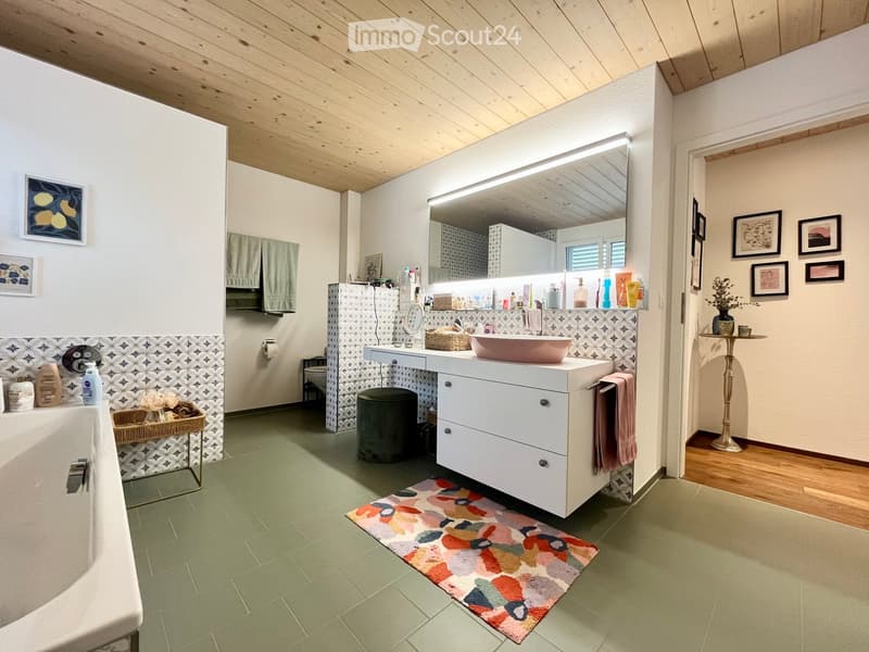 Bathroom with a bathtub, sink, vanity, mirror, and decorative items. Features a colorful rug, patterned tiles, and framed artwork on the walls.