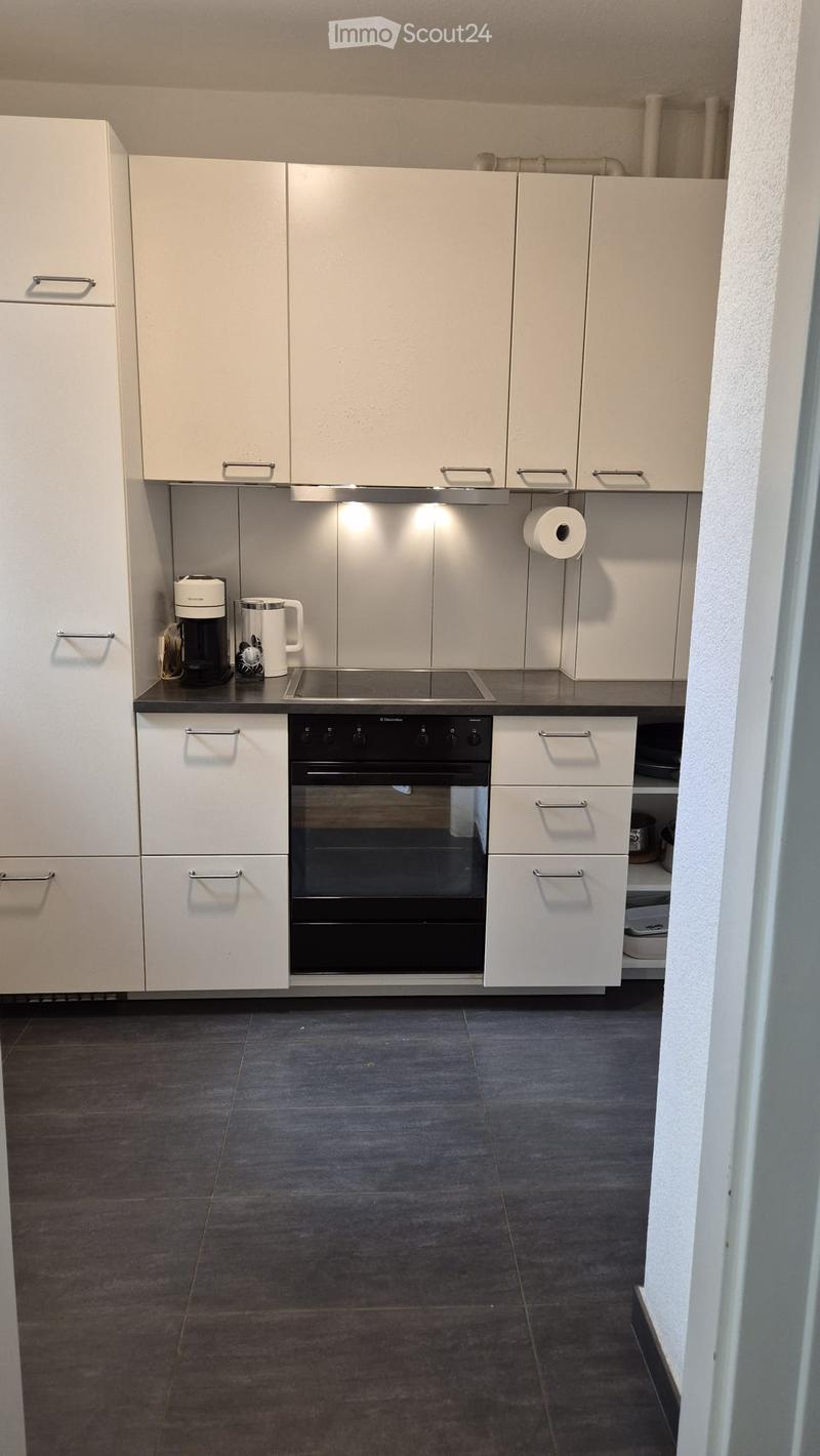 Modern kitchen with white cabinets, stainless steel appliances, and dark grey tiles.
