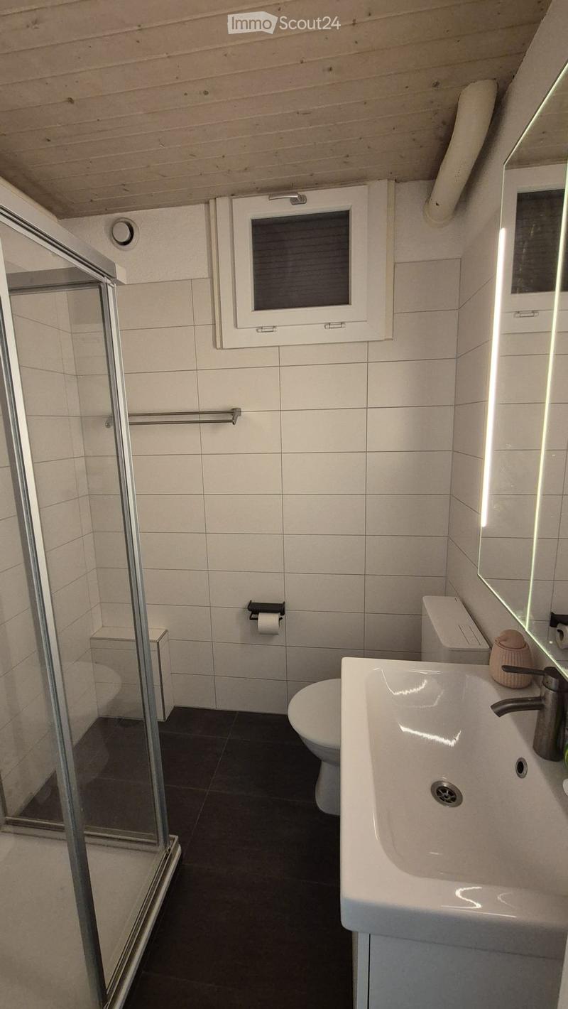 Modern bathroom with white tiles, a white sink with a modern faucet, a toilet, a shower stall with a glass door, and a mirror above the sink.