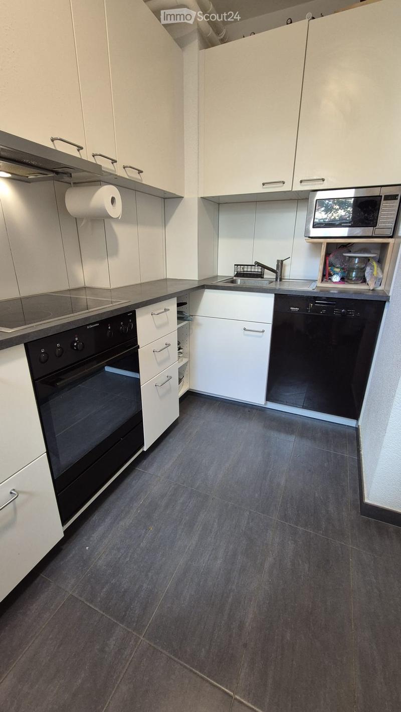 Modern kitchen with white cabinets, dark grey tiled floor, stainless steel appliances including oven, microwave, dishwasher, and sink.
