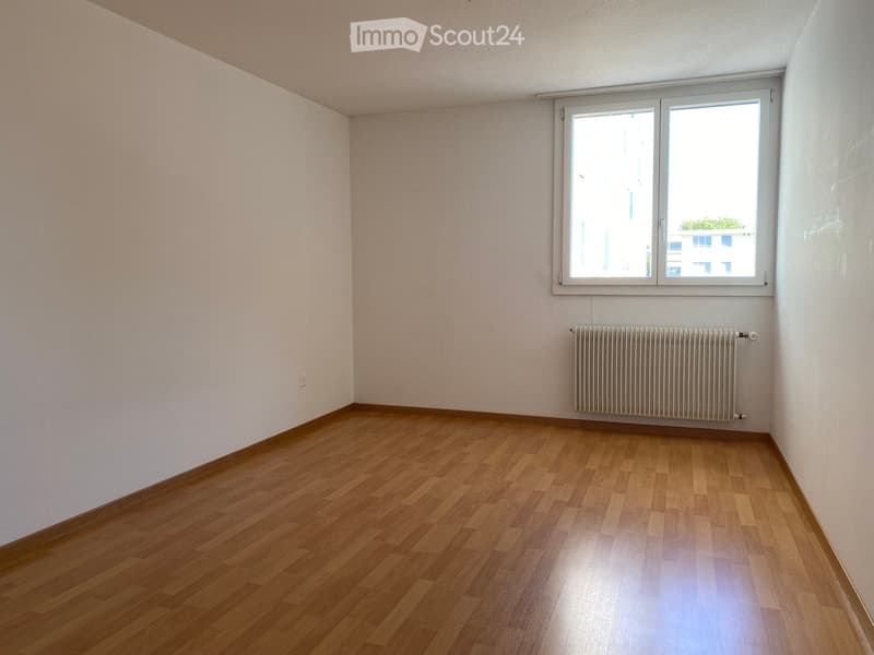 Empty room with wooden flooring, white walls, a window, and a radiator.