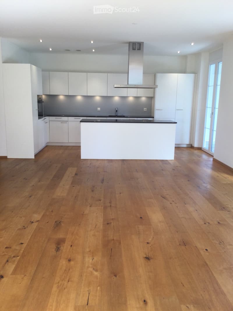 Empty kitchen with white cabinets, a central island, and wooden flooring.