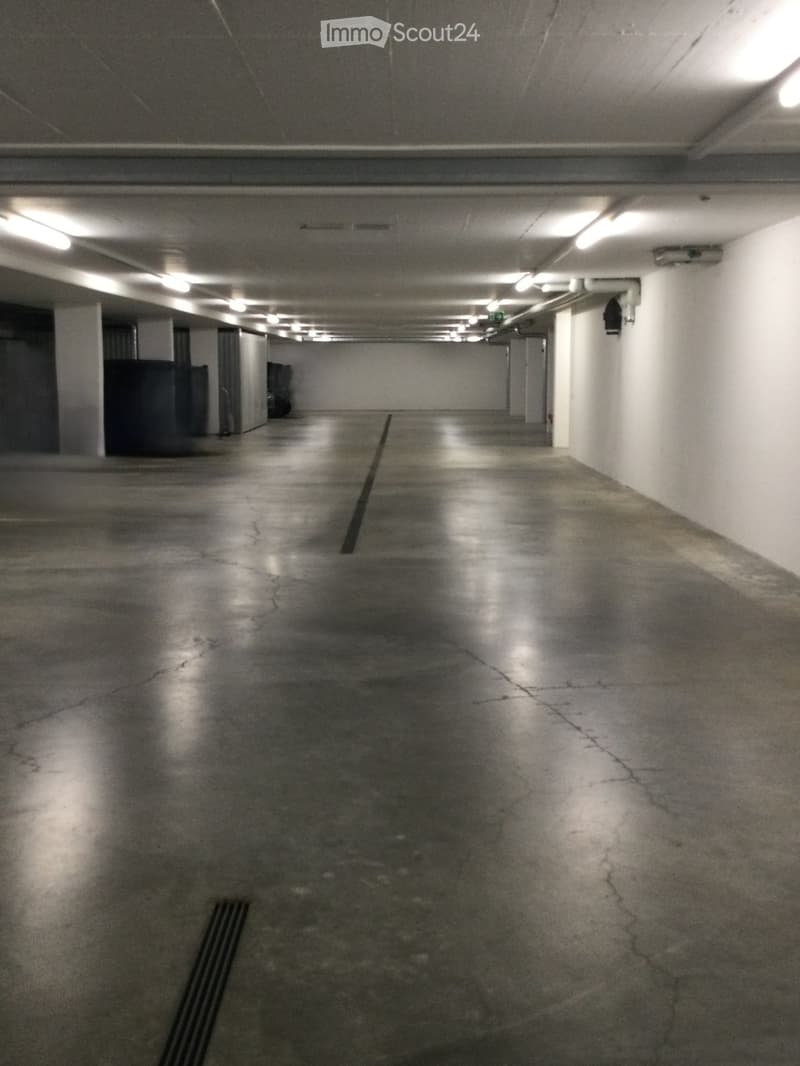 Empty underground parking corridor with concrete floors, white walls, and fluorescent lighting. No vehicles or furniture present.