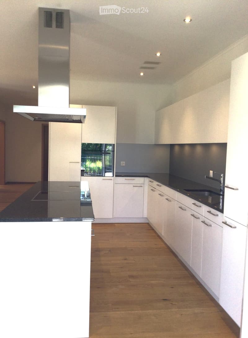Modern kitchen with white cabinets, dark countertops, and a central island. Features include a stainless steel range hood, a sink with a modern faucet, and recessed ceiling lighting.