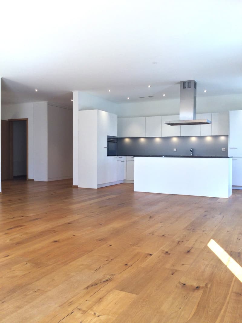 Modern kitchen with white cabinets, a central island, and a range hood. The floor is made of light wooden planks.