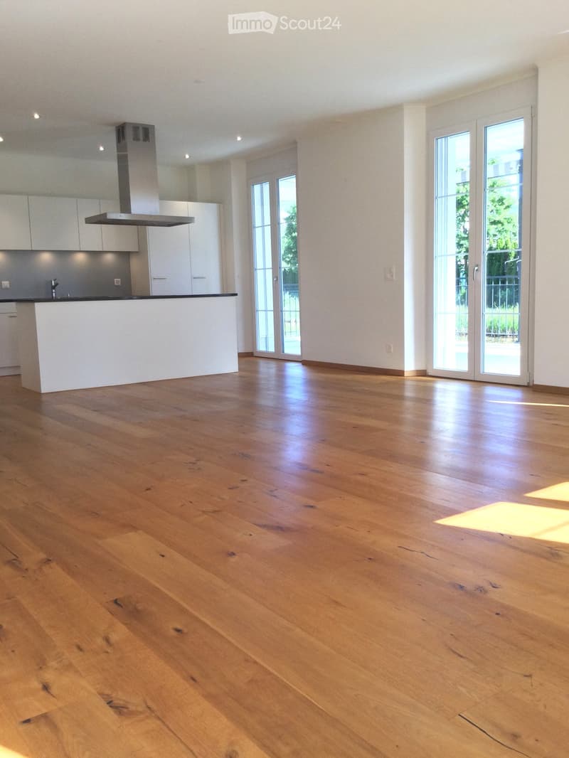 Open-plan kitchen and living area with light wooden flooring, white cabinetry, and large glass doors leading outside.
