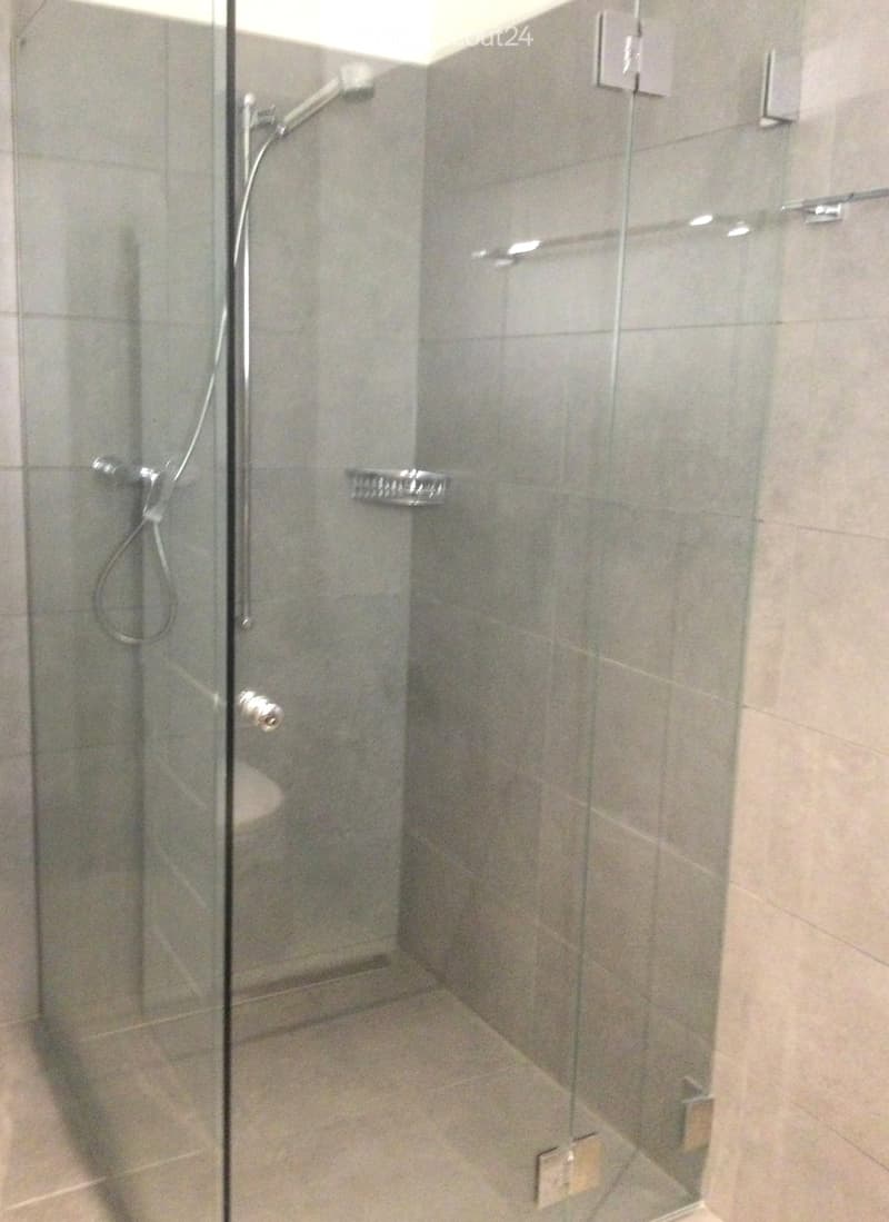 Modern shower area with glass enclosure, tiled walls, and multiple shower handles.