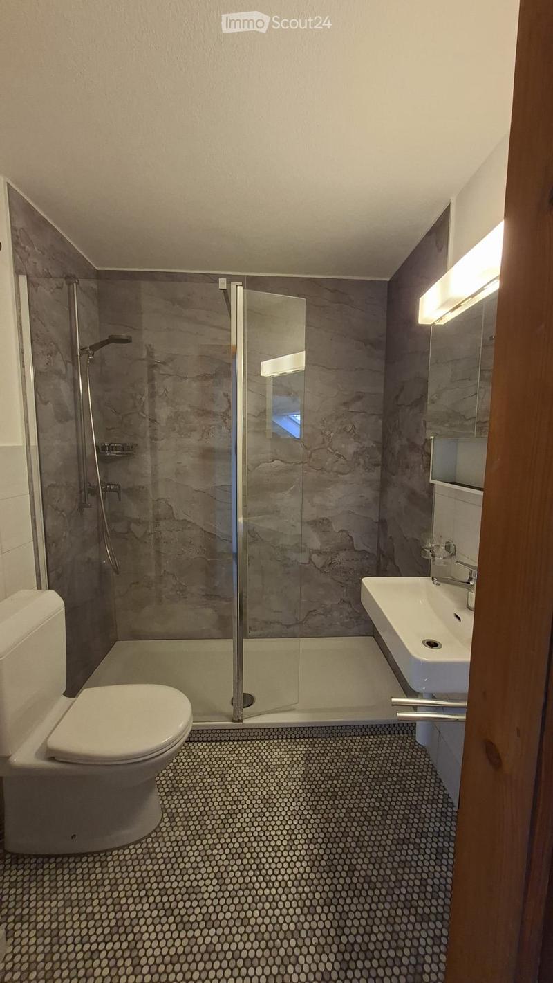 Modern bathroom with a white toilet, sink, and glass-enclosed shower. The walls are tiled in a marble-like pattern, and the floor features a circular mosaic tile design.