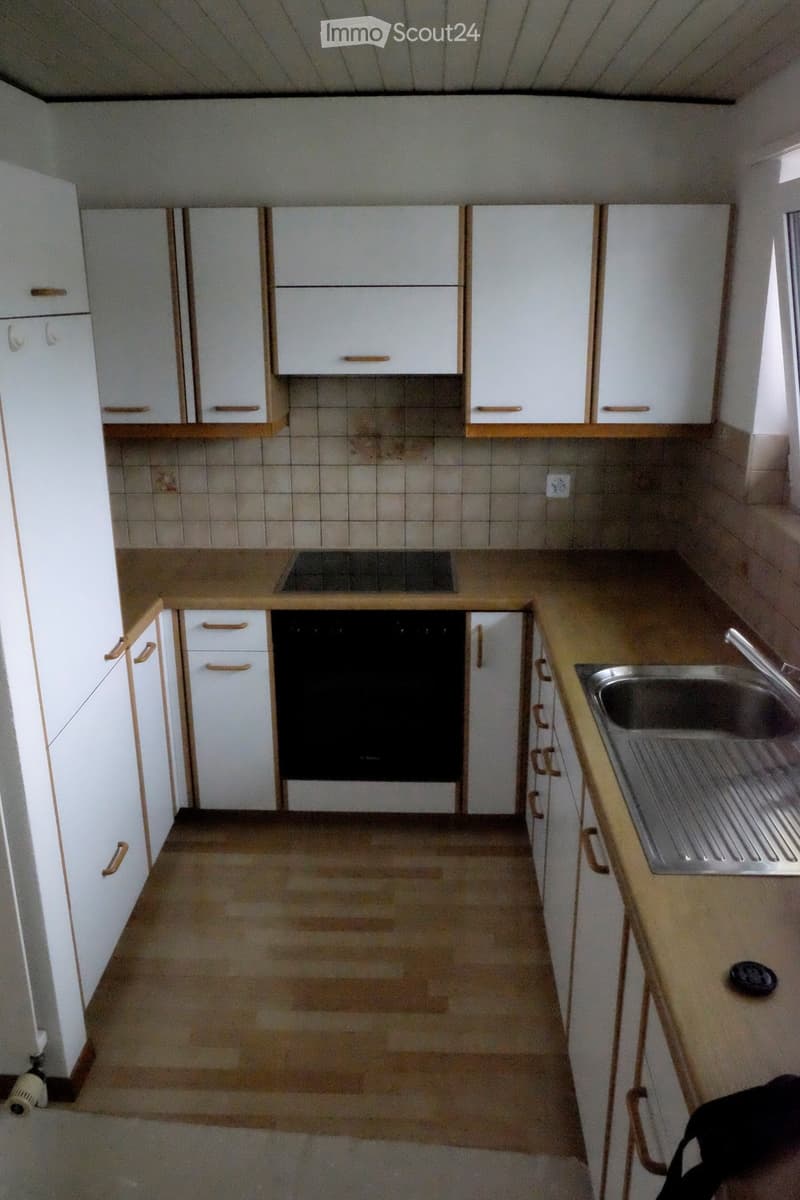Empty kitchen with white cabinets, a sink, and an oven. The countertops are light-colored, and the floor is tiled.
