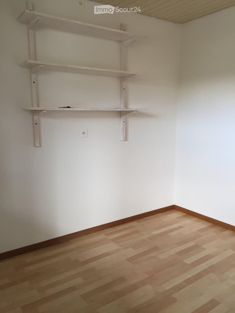 Empty room with light wooden flooring and white walls, featuring built-in white shelves on one wall.