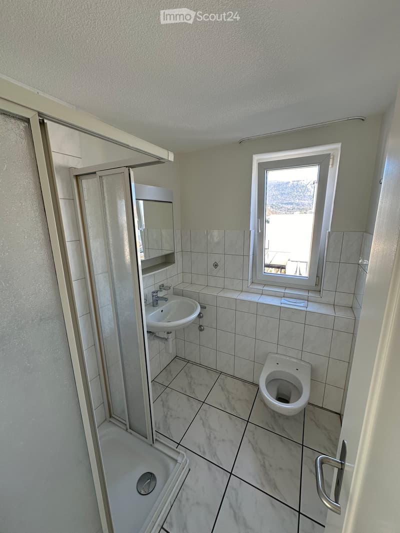 Modern bathroom with marble tiles, a sink, toilet, bathtub, and a window offering a scenic view.