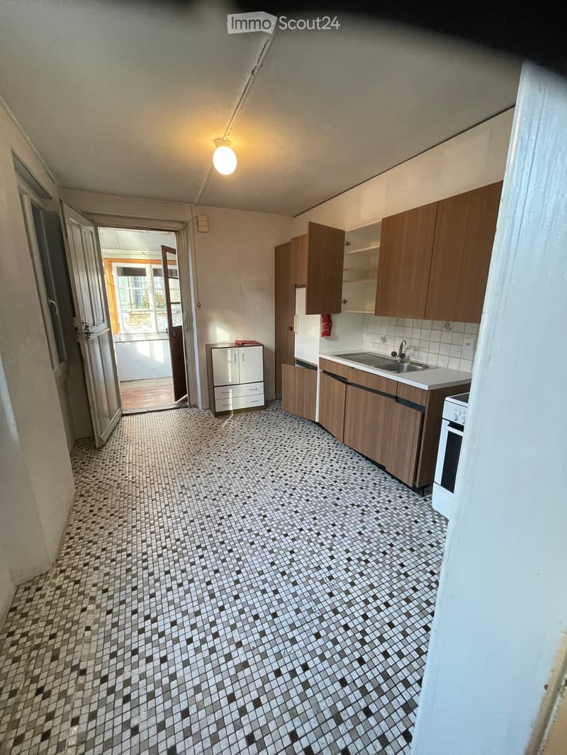 Kitchen with tiled floor, wooden cabinets, sink, faucet, oven, and refrigerator. Open doorway leads to another room.