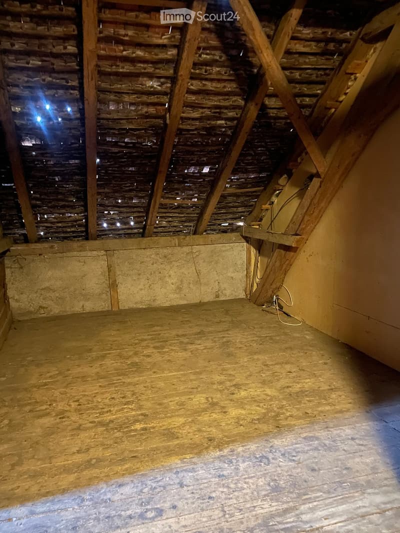 Empty attic space with wooden floor, exposed wooden beams, and brick walls. No furniture or equipment present.