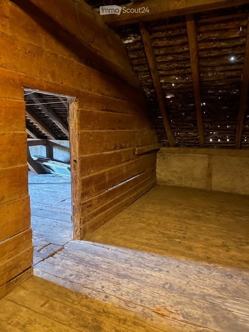 Empty attic space with wooden floors, exposed wooden beams, and brick walls. No furniture or equipment present.