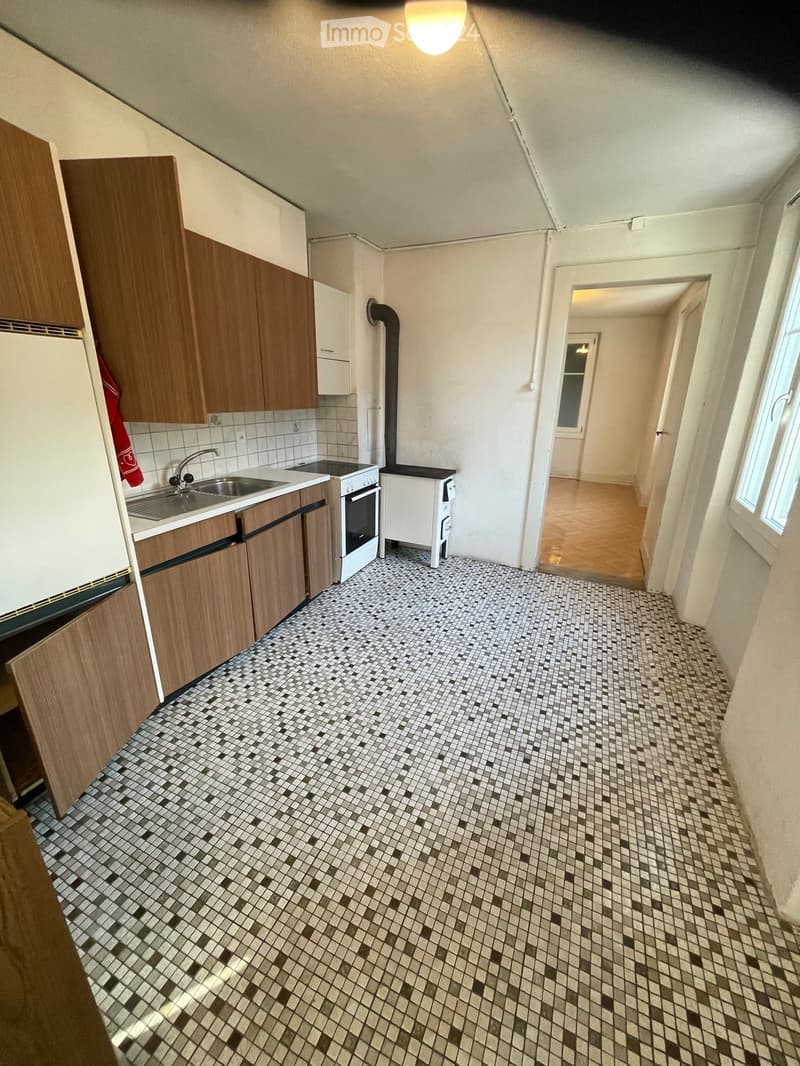 Kitchen with wooden cabinets, a sink, an oven, and a tiled floor. A doorway leads to another room.
