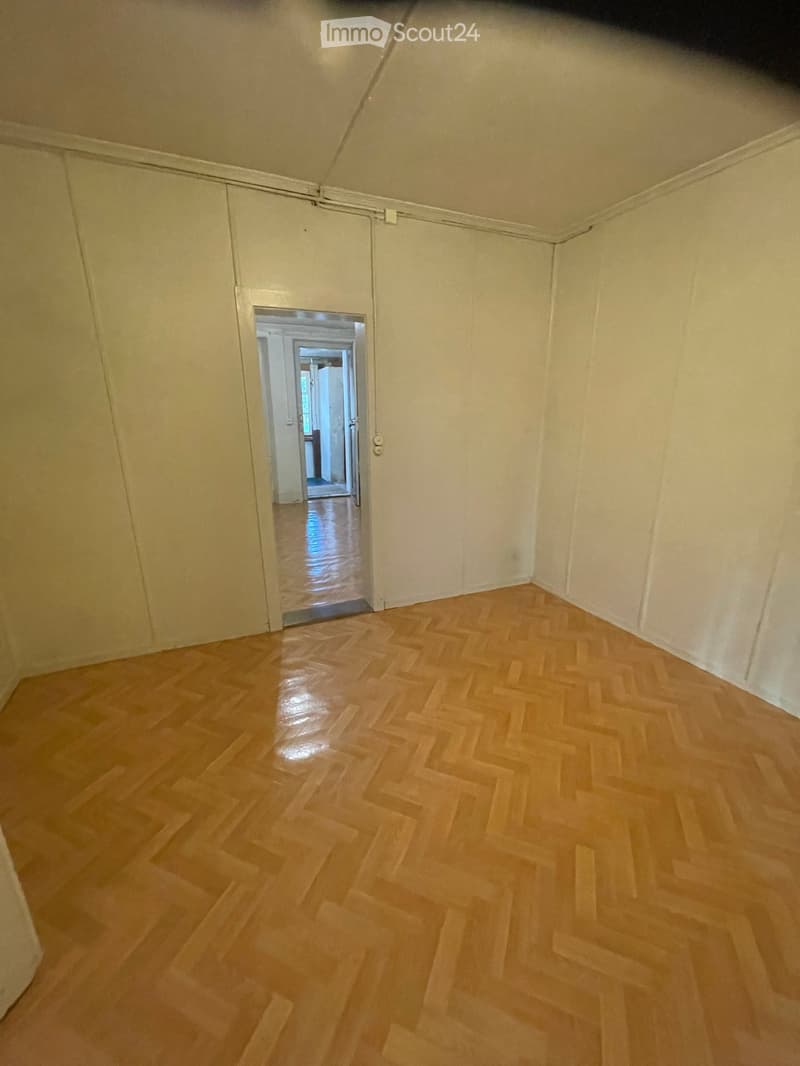 Empty room with light wooden herringbone flooring and white walls, featuring an open doorway leading to another room.