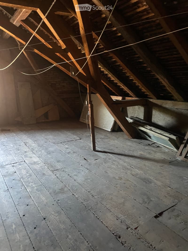 Empty attic space with exposed wooden beams and a concrete floor, showing some wear and tear.