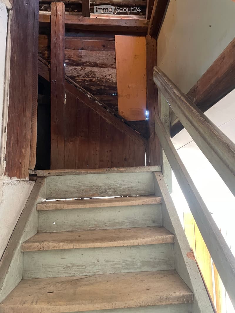 Wooden staircase with worn steps and handrails, leading upwards in a narrow hallway.