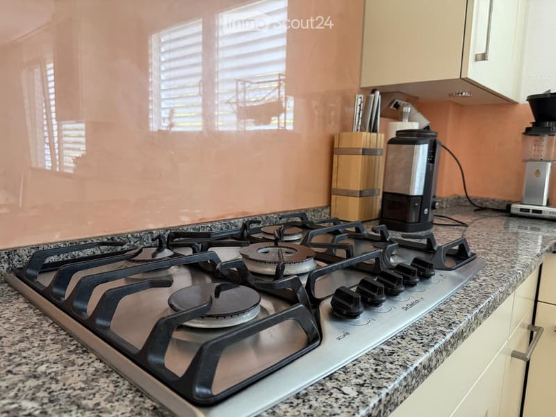 Modern kitchen with a gas stove, granite countertop, coffee maker, blender, and knife block.