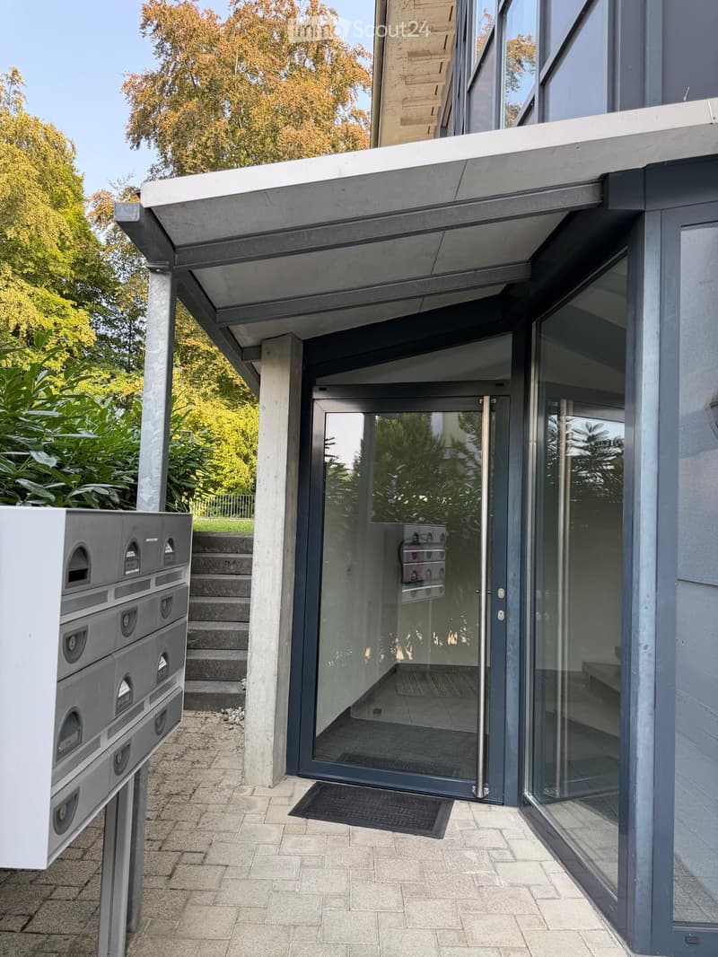 Modern building entrance with glass doors, mailboxes, and steps leading up to the entrance.