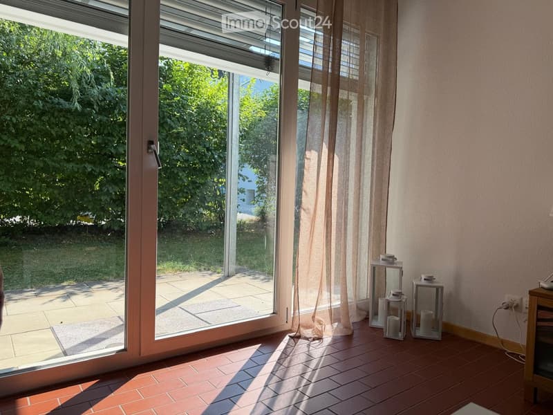 Bright room with large sliding glass door leading to a patio, tiled floor, sheer curtains, small table with lanterns.