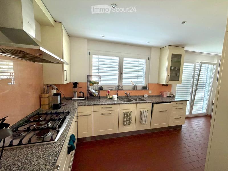 Modern kitchen with white cabinets, granite countertops, a four-burner stove, and a double sink. Features include a built-in range hood, a window with blinds, and a tiled floor.