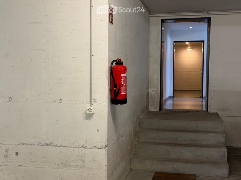 Concrete staircase leading to an open doorway, with a red fire extinguisher mounted on the wall and a visible electrical outlet.