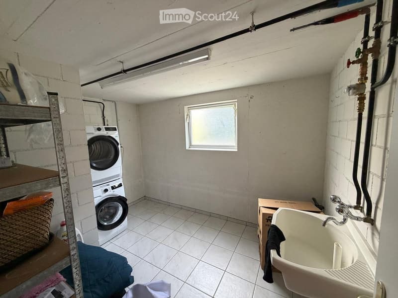 Utility room with a washing machine, sink, and shelves. The room has exposed brick walls and a small window.