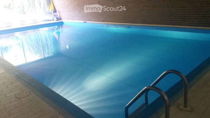 Indoor swimming pool with clear blue water, tiled edges, and a metal handrail on one side.
