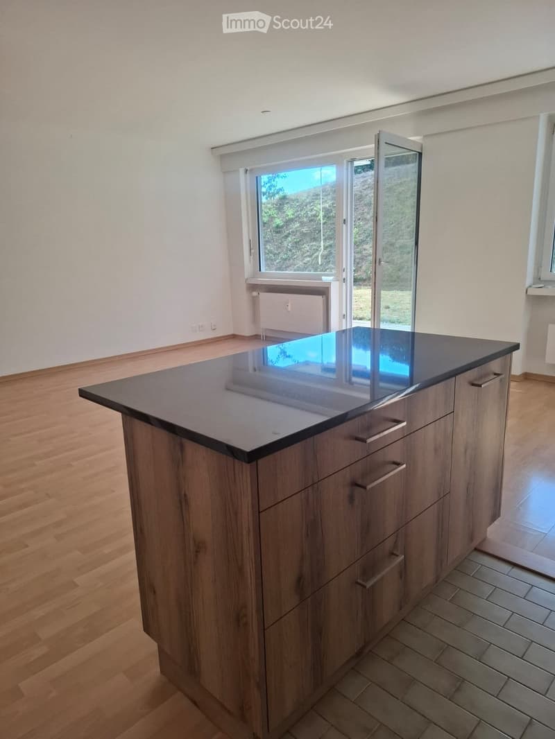 Modern kitchen with a wooden island and dark countertop, large windows and sliding doors leading to a garden.