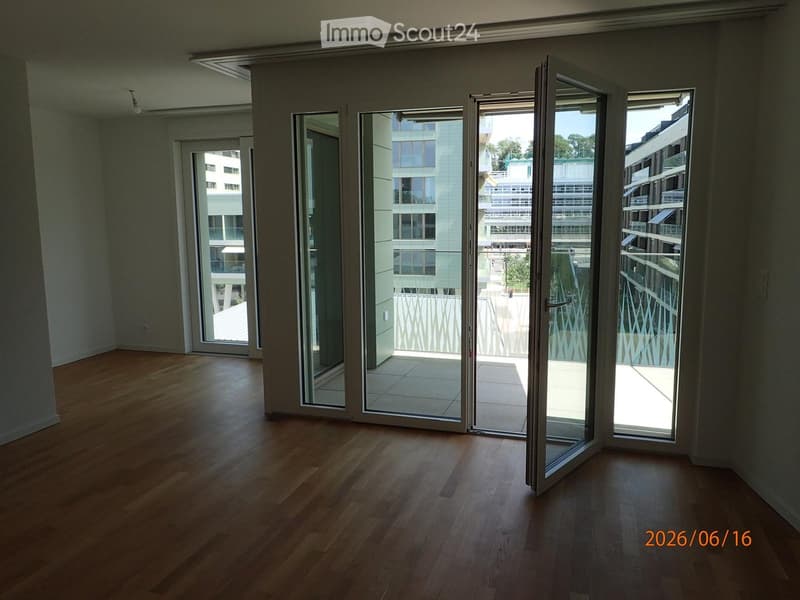 Empty room with wooden flooring, large glass sliding doors leading to a balcony, and neutral-colored walls.