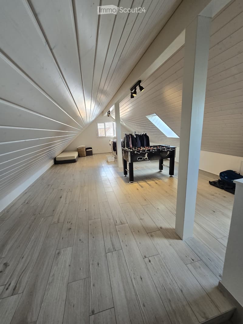 Attic room with wooden flooring, slanted ceilings, and skylight windows. Features a foosball table, clothing rack, and small seating area.