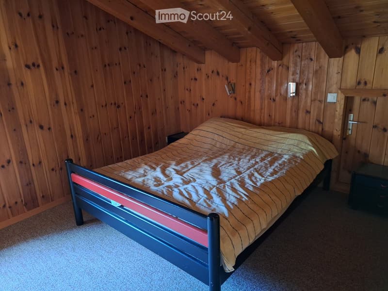 Cozy attic bedroom with wooden walls and slanted ceiling, featuring a single bed with striped bedding and a nightstand.
