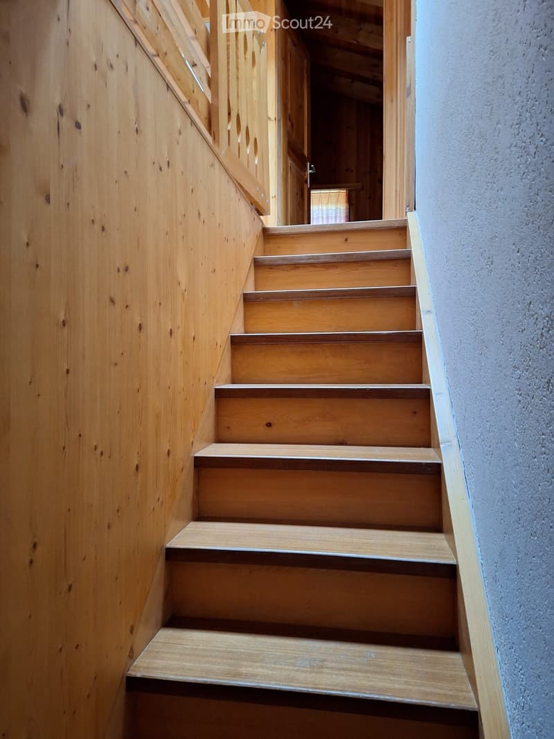 Wooden staircase with a wooden handrail and a grey wall on the right side.