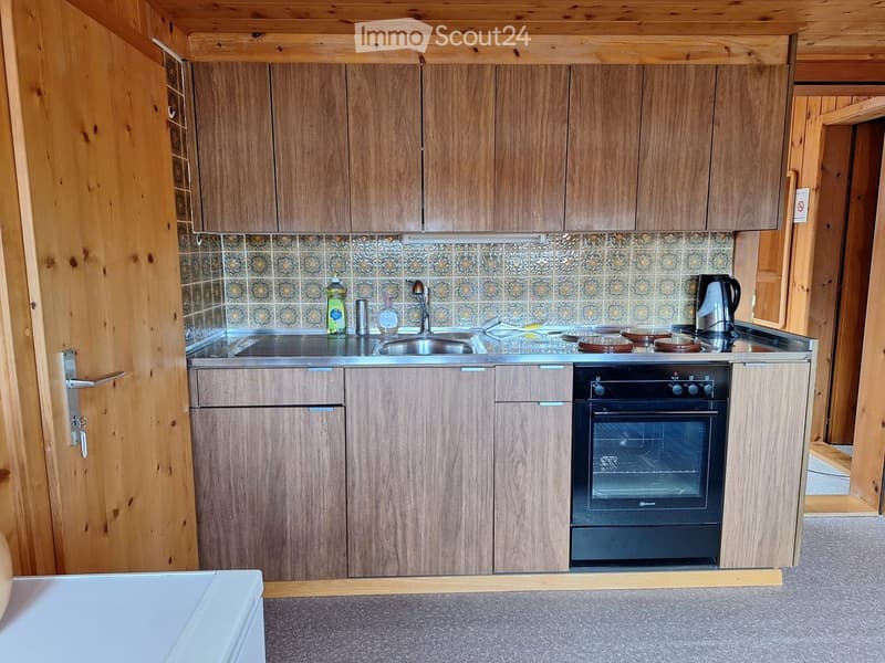 A compact kitchen with wooden cabinets, a stainless steel sink, and a built-in oven. The backsplash features a decorative tile pattern.