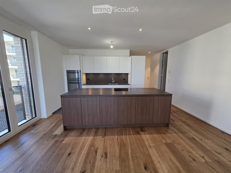 Modern kitchen with light wood flooring, white cabinets, a central island, and built-in appliances including an oven and sink.