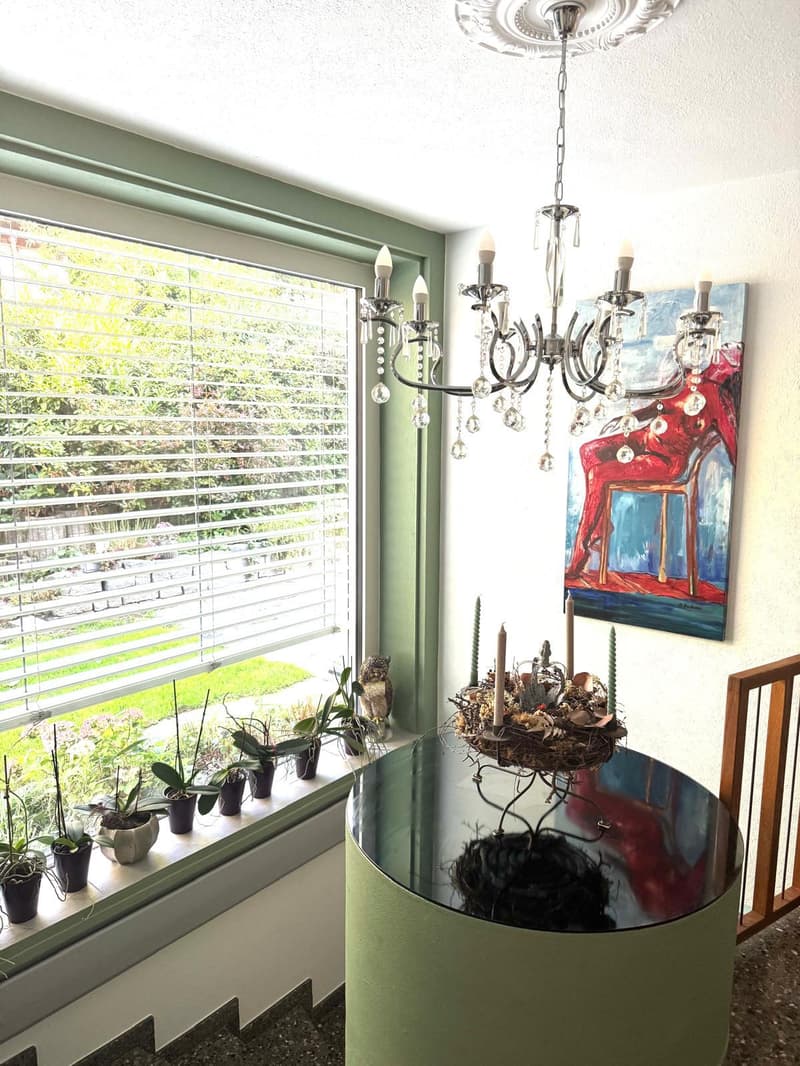 decorated table, chandelier, painting, plants, window, hardwood stairs