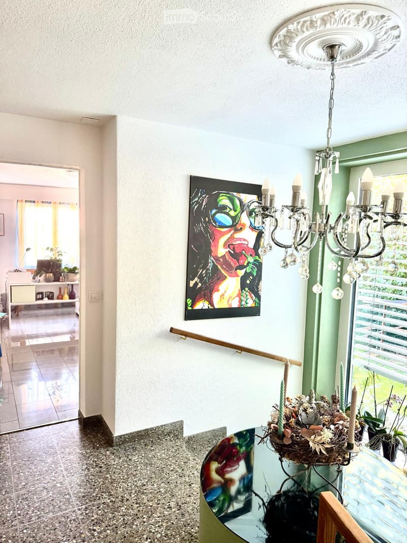 Entrance hall with tile flooring, a chandelier, a painting, a wooden handrail, a glass table, and candles.