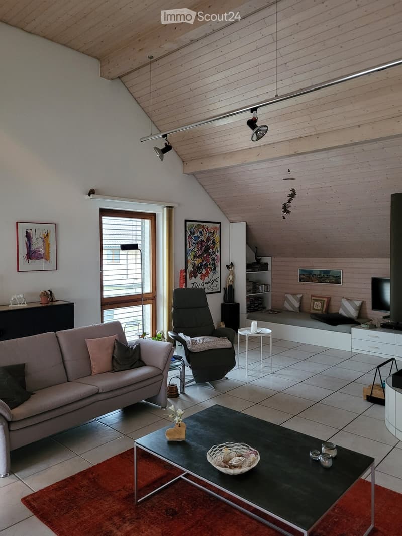 Modern living room with wooden slanted ceiling, large window, sofa, coffee table, armchair, small table, shelf, and television.