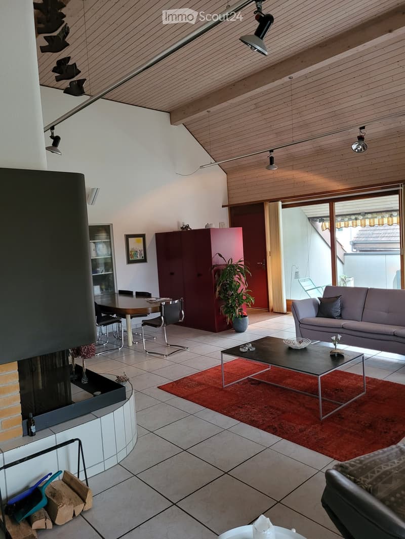 Modern living room with a fireplace, sofa, coffee table, dining area, and large windows leading to a balcony.